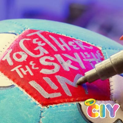 person using Crayola metallic marker to decorate soccer ball panel